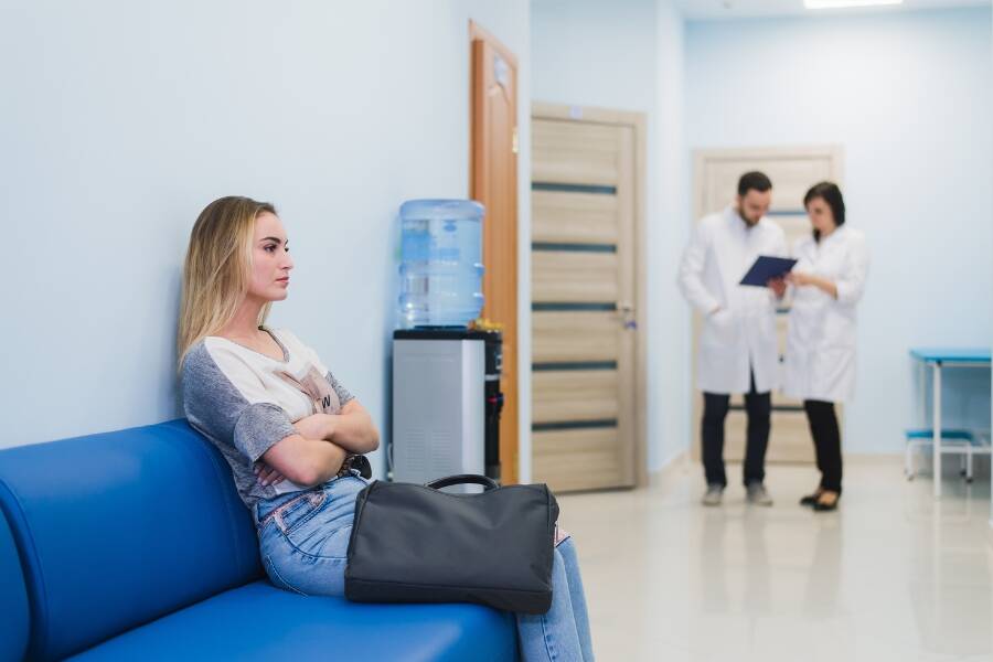 A woman patient sitting in a hospital's waiting room, illustrating patient wait times and clinic workflow delays