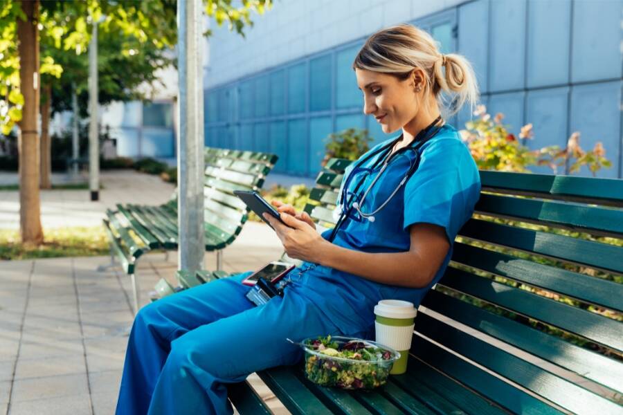 A female doctor in scrubs sitting on a bench, looking thoughtful and relaxed in a medical setting.