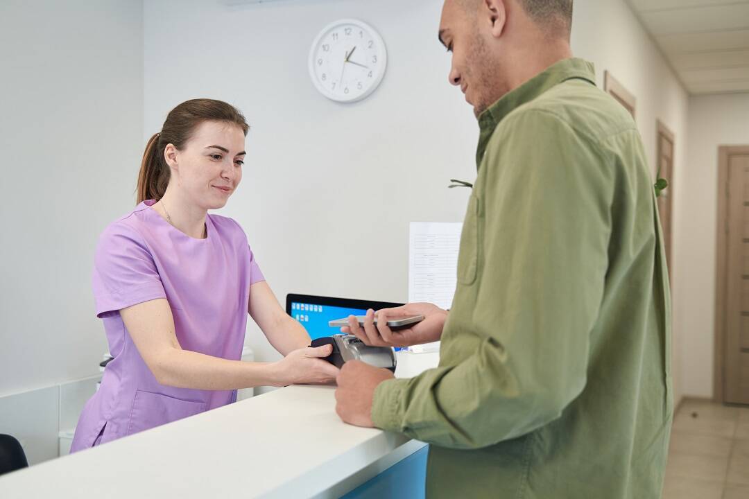 Receptionist facilitating patient collections with patient via card terminal